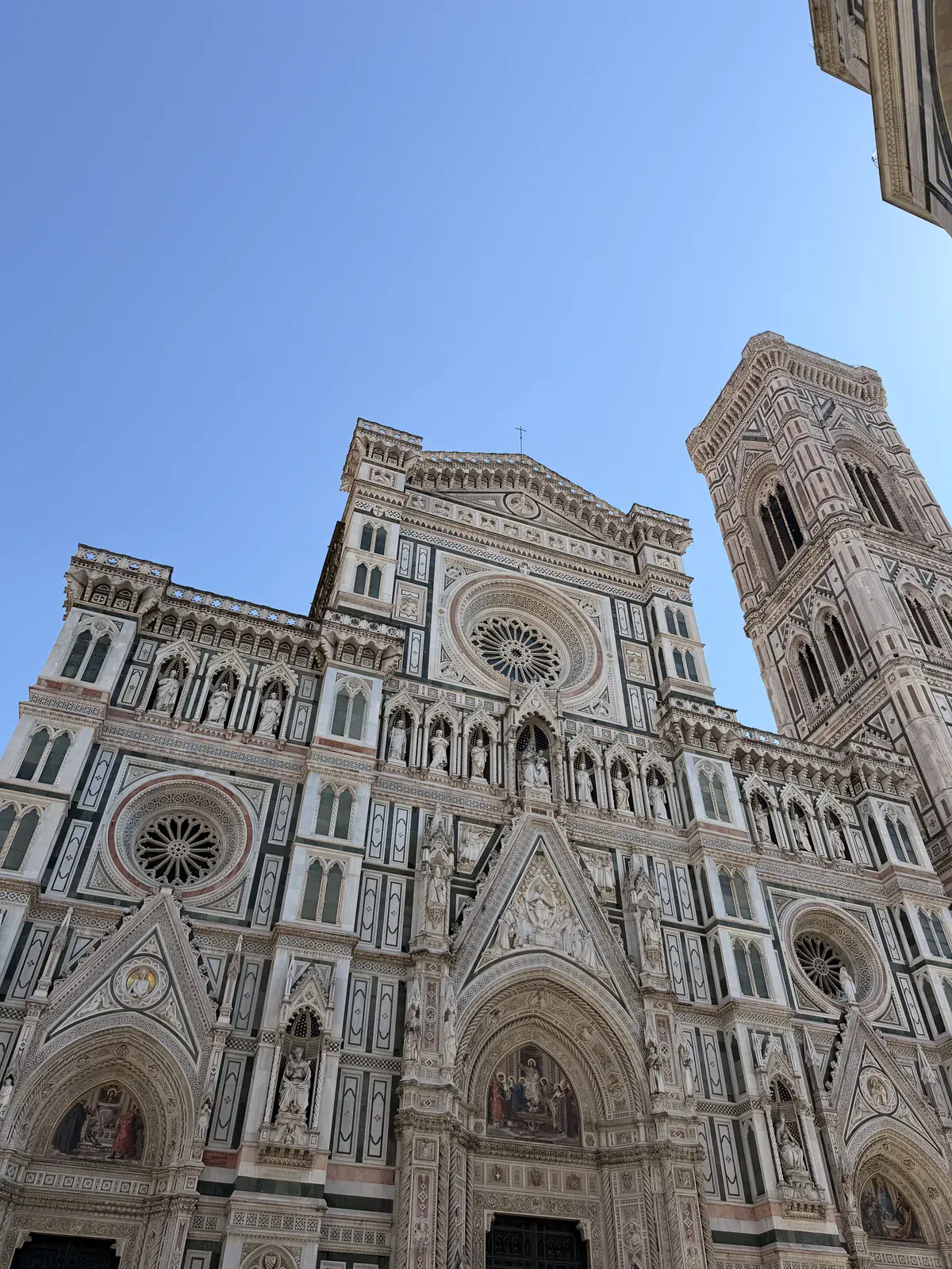 The green, white and pink marble facade of Florence Cathedral and Giotto's bell tower seen from the square below against a clear sky