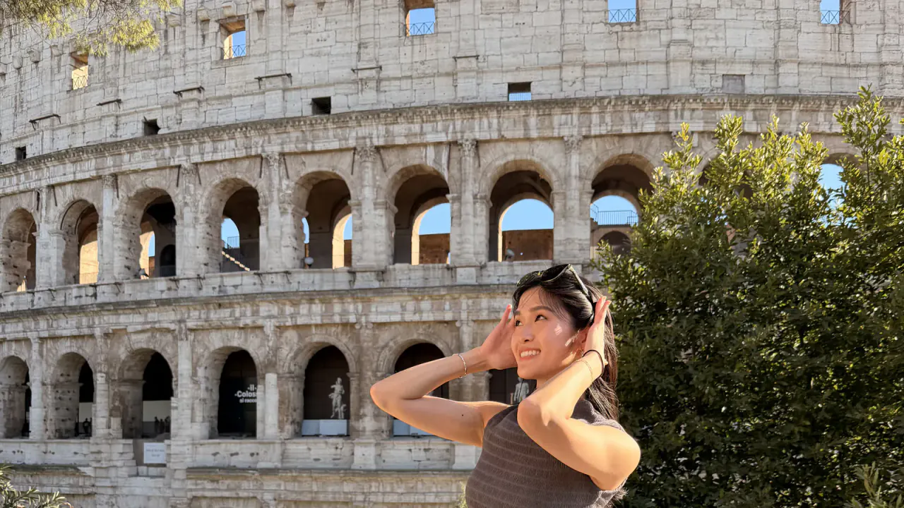 A traveler posing in front of the Colosseum's arched exterior in Rome