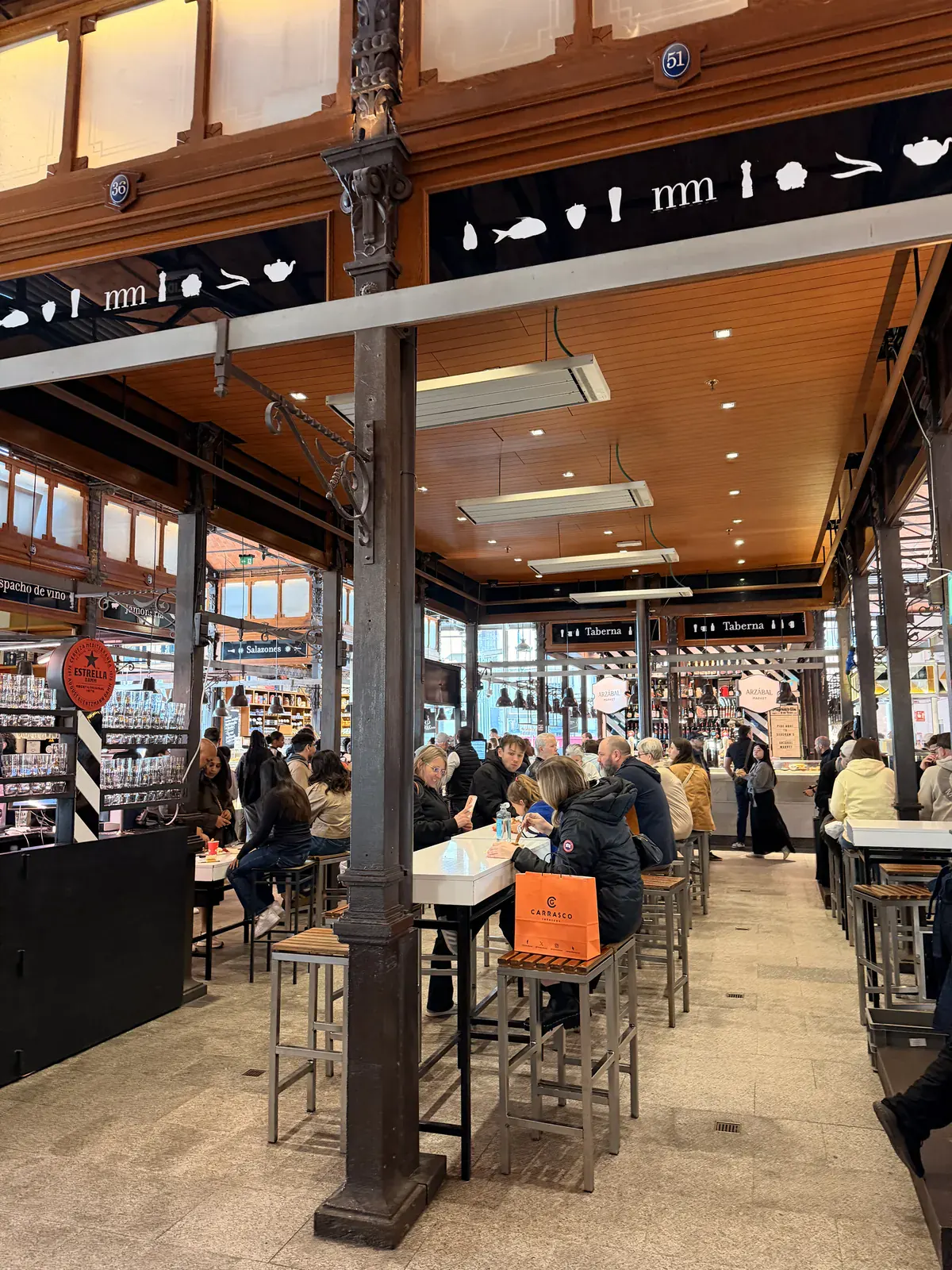 Diners at high tables under the iron columns and glass walls of Mercado de San Miguel in Madrid.