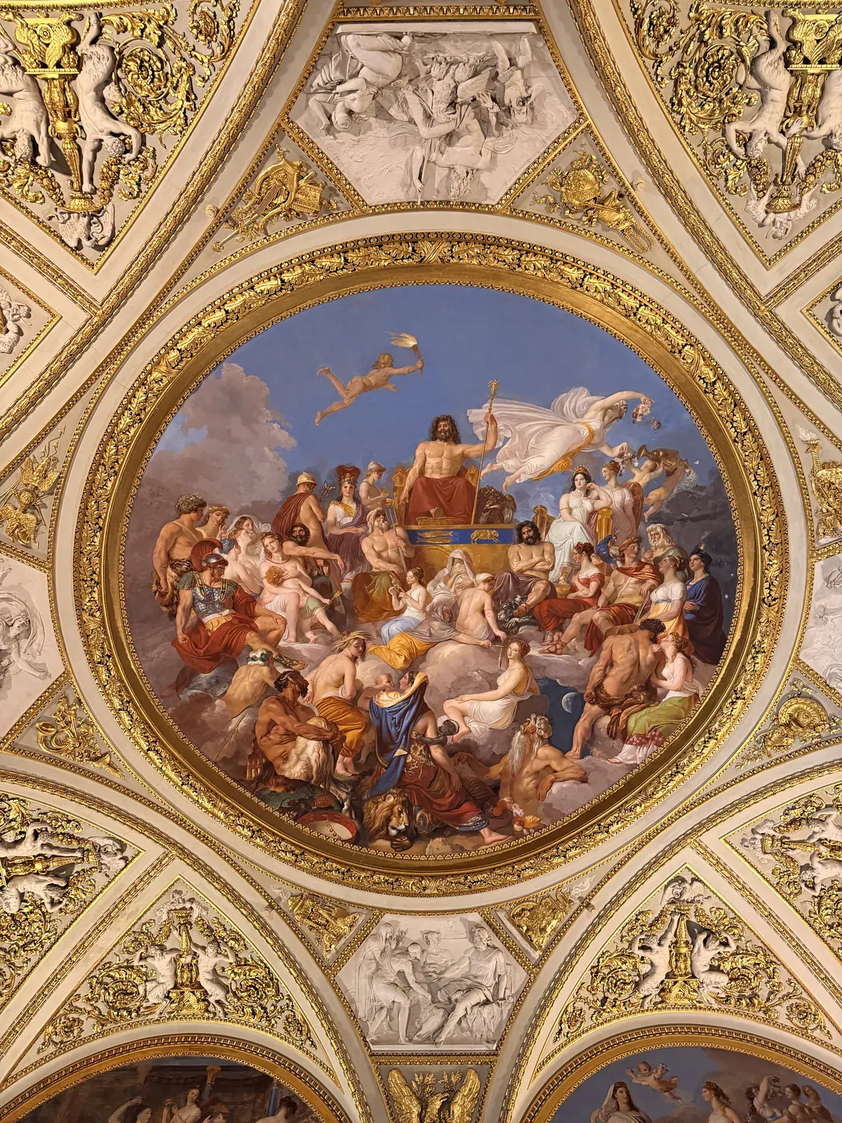 An ornate gallery inside Palazzo Pitti lined with framed paintings, gilded decoration and chandeliers
