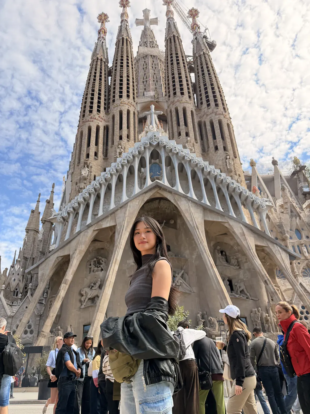 A woman standing in front of the carved Passion façade and spires of the Sagrada Família in Barcelona.