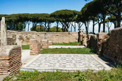 Ancient brick ruins and a geometric mosaic floor beneath umbrella pines at Ostia Antica